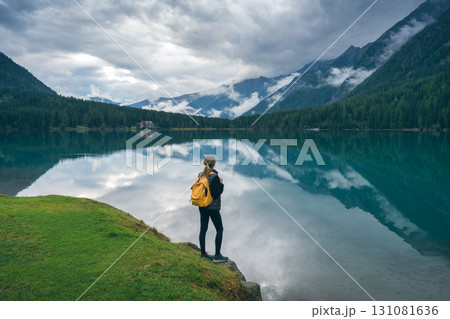 Woman with yellow backpack standing near lake in mountains 131081636
