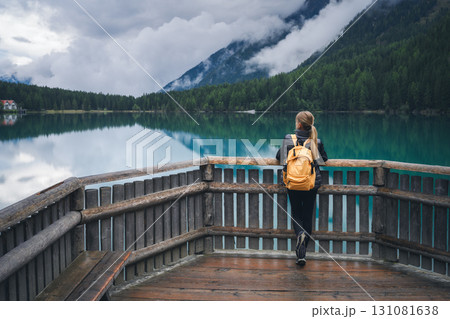 Woman with yellow backpack standing on wooden terrace near lake Woman with yellow backpack standing on wooden terrace near lake 131081638