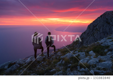 Two women hikers with backpacks standing on mountain at sunset 131081640