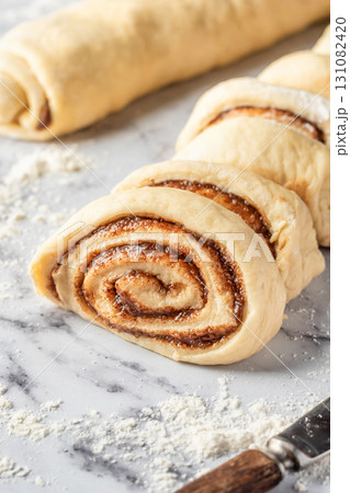 Cutted roll of dough on white marble background. Making cinnamon rolls process. Cinnabon preparation 131082420