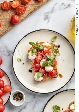 Caprese sandwich or toast with mozzarrella balls, cherry tomatoes, olive oil and fresh basil leaves top view close up on white marble background 131082424