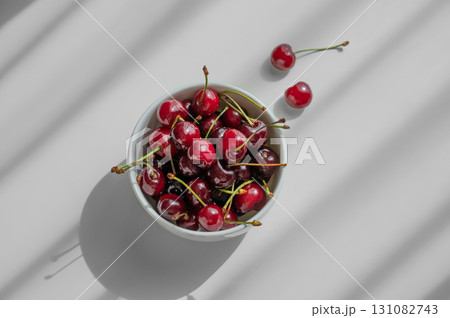 Bowl with fresh red cherry on white background with sunny light and shadows. Bowl with fresh red cherry on white background with sunny light and shadows. 131082743