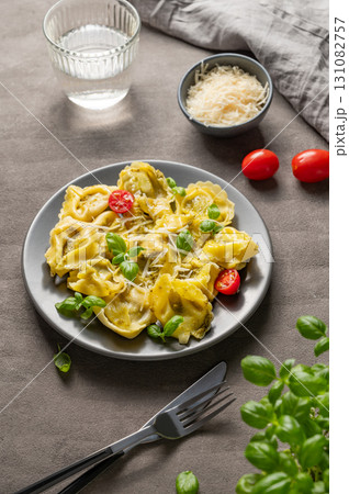 Tortellini pasta with parmesan, pesto and basil in a plate on a dark background with glass of water Tortellini pasta with parmesan, pesto and basil in a plate on a dark background with glass of water 131082757