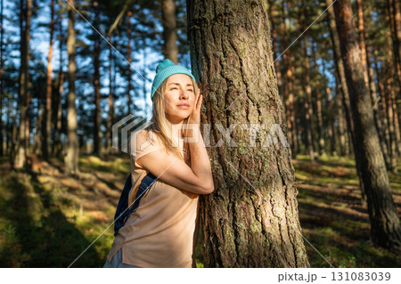 Loving nature purity. Relaxed thoughtful woman touching tree trunk in autumn forest at sunset. 131083039