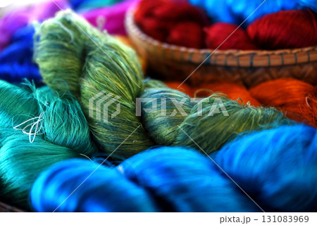 Tie of colorful and shiny beautiful silk yarn dyed placed in a pile of round bamboo baskets. Prepared for use as a raw material for weaving silk. 131083969