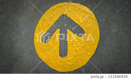 rustic bold yellow arrow points upward inside a circle, stamped on rough dark pavement. Conveys direction, progress, and guidance perfect for visuals about growth, navigation, or decision-making in 131086956