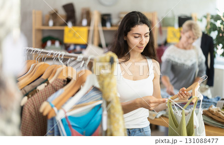 Young woman customer elect something summer clothes in store. Female client choosing something in background Young woman customer elect something summer clothes in store. Female client choosing something in background 131088477