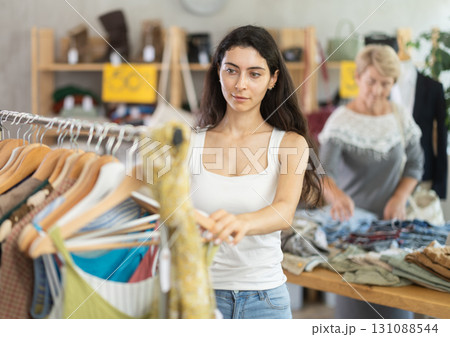 Young woman customer elect something summer clothes in store. Female client choosing something in background 131088544