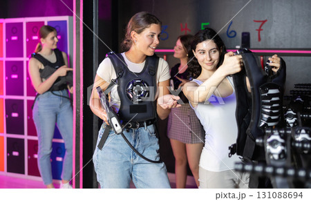 Girls try on a matching vest for playing laser tag in dark room 131088694