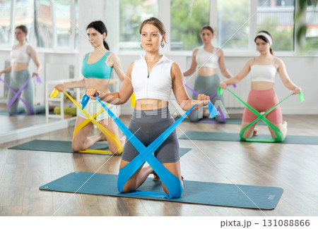Young woman performs exercises with resistance band during Pilates strength training, kneeling 131088866