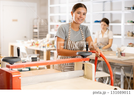 Girl student in pottery workshop works with machine clay press roller 131089011