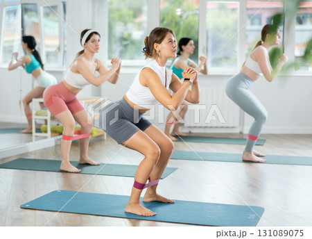 Young girls practicing half squat with band standing on mat 131089075