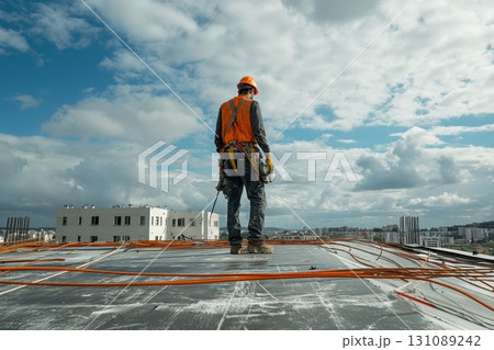 A man in an orange safety vest stands on a roof A man in an orange safety vest stands on a roof 131089242
