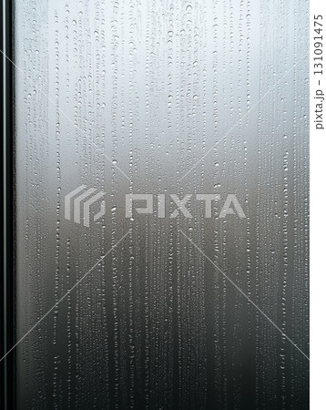 Detailed Close-up of Raindrops Sliding Down a Misty Glass Surface 131091475