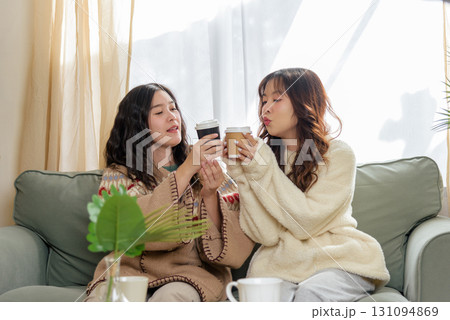 Winter day finds friends enjoying drinks at home, cozy friendship moments shared inside during winter cold, women relaxing in comfortable sweaters. 131094869