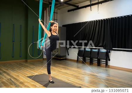 Woman practicing aerial yoga pose with hammock, balancing gracefully in a fitness studio 131095071