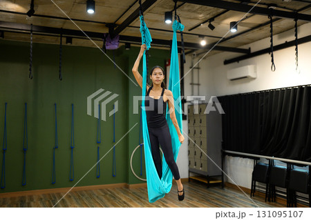 Female athlete standing confidently with aerial yoga swing, focusing on strength and balance training Female athlete standing confidently with aerial yoga swing, focusing on strength and balance training 131095107