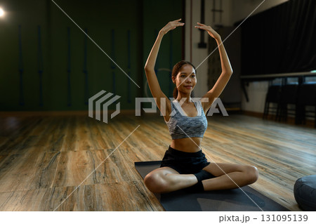 Woman practicing seated yoga pose with arms raised overhead on exercise mat in studio Woman practicing seated yoga pose with arms raised overhead on exercise mat in studio 131095139
