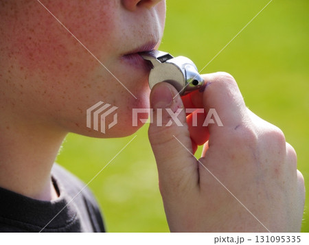 Young boy is holding a whistle in his mouth 131095335