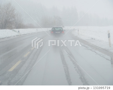 Car is driving down a snowy road with a lot of snow on the ground 131095719