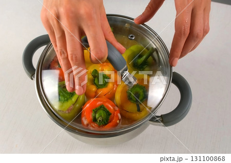 Chef woman cooks covering saucepan with stuffed bell peppers by lid on kitchen. Chef woman cooks covering saucepan with stuffed bell peppers by lid on kitchen. 131100868