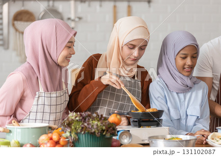 Muslim family cooking together in modern kitchen. Woman in hijab stirring food, child watching, and man preparing ingredients. Concept of halal food, family bonding, healthy lifestyle, and home Muslim family cooking together in modern kitchen. Woman in hijab stirring food, child watching, and man preparing ingredients. Concept of halal food, family bonding, healthy lifestyle, and home 131102087