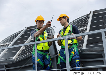 Two engineers in safety gear inspect rooftop cooling tower systems for building maintenance and energy optimization. Concept of HVAC technology, facility management, and industrial operation. 131102970