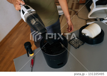 Cropped shot of cleaning company worker male cleaning air humidifier using handheld vacuum cleaner, performing thorough home device maintenance for optimal indoor air quality and cleanliness. 131105495