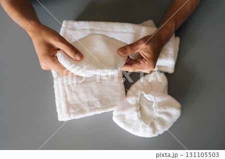 Closeup top view of man holding soft white microfiber cleaning pad, showcasing textured surface near cleaning supplies on gray background. Concept of hygiene and cleanliness in domestic environment. 131105503