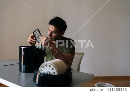 Man holding and inspecting air humidifier filter, performing maintenance and cleaning to ensure clean and healthy air in home environment. Concept of maintenance modern home appliance. 131105526