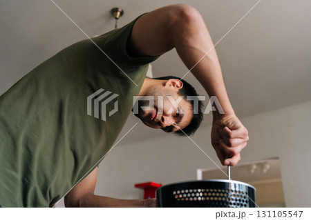 Vertical portrait of focused technician disassembling modern black air humidifier, revealing internal components and filter during maintenance work with screwdriver on clean surface. 131105547