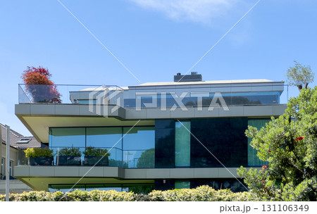 Villa with glass facade. Modern luxury house with balcony, minimalist design, greenery, garden, tree 131106349