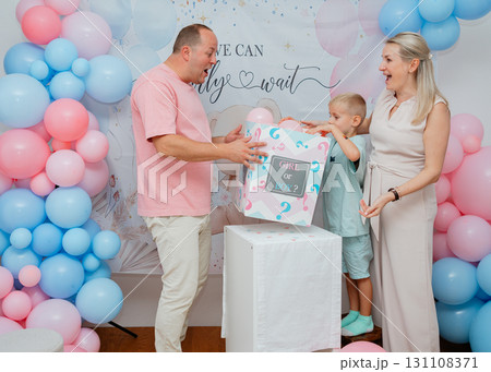 Parents and child open decorated box at baby shower, pink and blue balloons create festive atmosphere. Useful for party marketing, family lifestyle blogs and maternity visuals Parents and child open decorated box at baby shower, pink and blue balloons create festive atmosphere. Useful for party marketing, family lifestyle blogs and maternity visuals 131108371