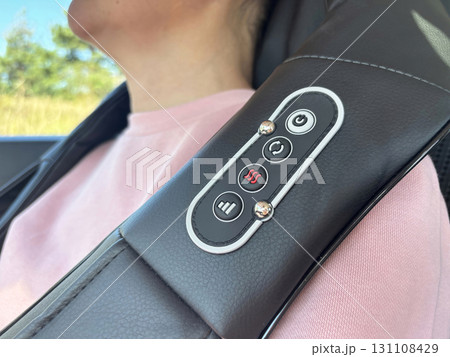 A woman enjoys a massage with an electric massager in a car. Relaxation during a long drive or trip, portable massage device for neck and shoulders, health and wellness lifestyle 131108429