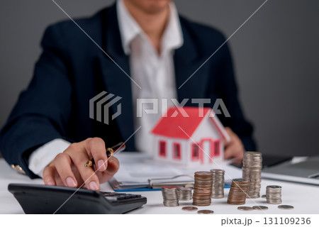 Businessman calculating home loan or mortgage investment with coin stack and house model, real estate finance planning budget and banking services. Businessman calculating home loan or mortgage investment with coin stack and house model, real estate finance planning budget and banking services. 131109236
