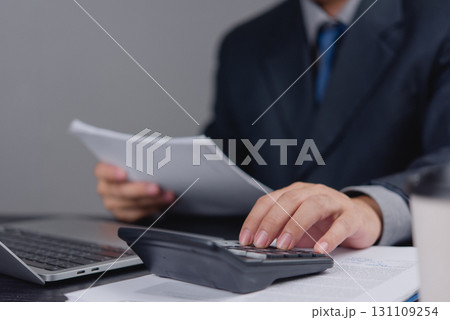 Businessman using calculator to review financial documents, representing accounting, expense tracking, and budget planning for business. tax filing auditing, and money management. 131109254
