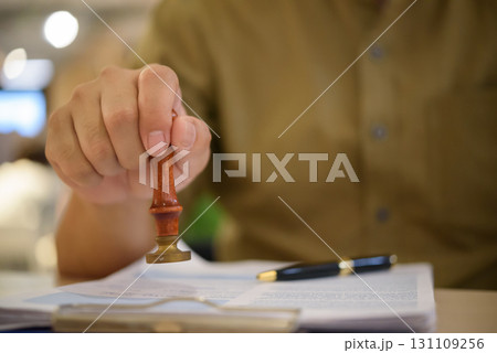 Hand using a rubber stamp on official papers, representing approval process, legal documentation, and certified paperwork. contract certification, notarization, and business authorization. 131109256