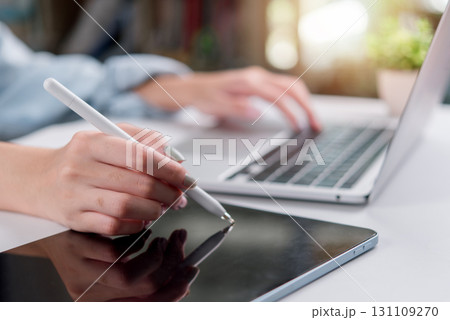 person using a tablet with a stylus and a laptop, showcasing digital design, productivity, and modern technology in a creative workspace. person using a tablet with a stylus and a laptop, showcasing digital design, productivity, and modern technology in a creative workspace. 131109270