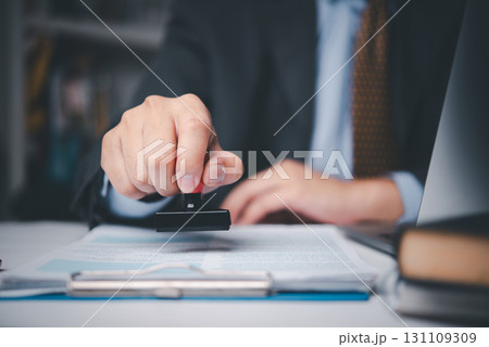 Businessman stamping contract document on desk, symbolizing legal approval, corporate agreement, and business authorization process. 131109309
