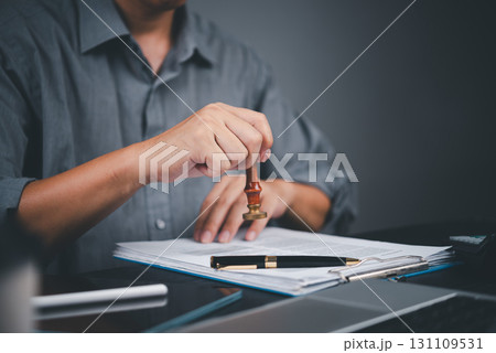 Hand using a rubber stamp on official papers, representing approval process, legal documentation, and certified paperwork. contract certification, notarization, and business authorization. 131109531