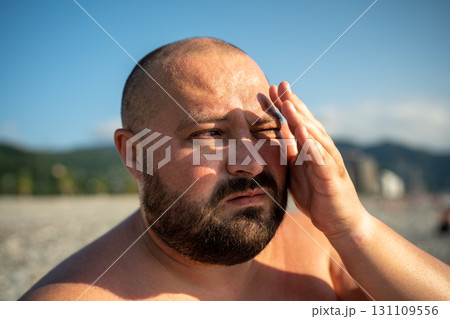 Bearded overweight man looking at distance on nature at sunny weather covering eyes from sun. Bearded overweight man looking at distance on nature at sunny weather covering eyes from sun. 131109556