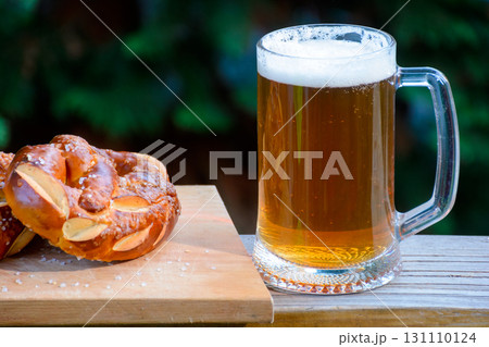 having beer and pretzel outdoors. celebrate oktoberfest. glass mug with cold beverage on the dark background of garden. rustic scene having beer and pretzel outdoors. celebrate oktoberfest. glass mug with cold beverage on the dark background of garden. rustic scene 131110124