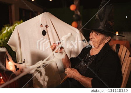 Senior woman wearing witch costume holding spider web with ghost at Halloween party Senior woman wearing witch costume holding spider web with ghost at Halloween party 131110589