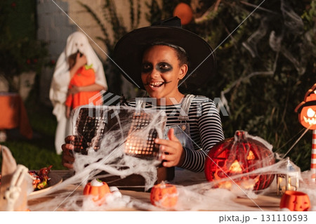 Girl wearing witch costume holding a spider web covered box at Halloween party Girl wearing witch costume holding a spider web covered box at Halloween party 131110593