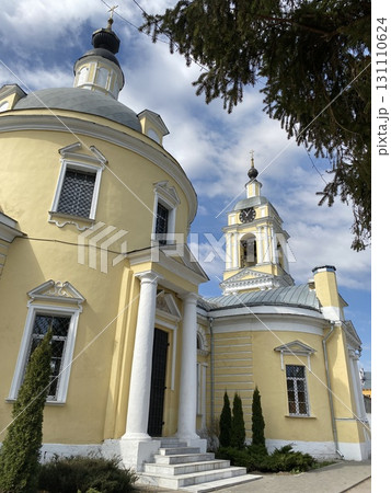 Orthodox church with bell tower under blue sky, featuring vivid yellow facade and white accents 131110624