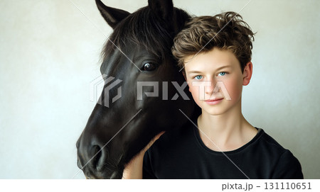 Teen boy gently holding black horse's head, both looking at camera against soft neutral background 131110651