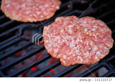 Raw burger patties on grill over hot coals 131110717
