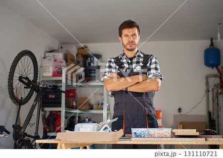 Carpenter standing with crossed arms in home workshop with tools and materials Carpenter standing with crossed arms in home workshop with tools and materials 131110721