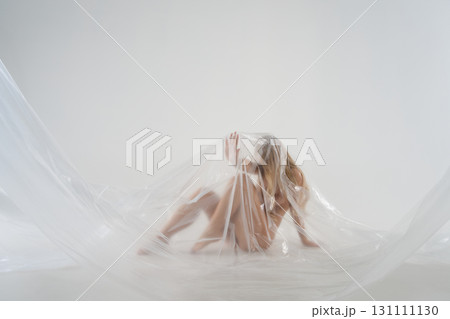 Blonde woman in a studio wrapped in plastic for a beauty session Blonde woman in a studio wrapped in plastic for a beauty session 131111130