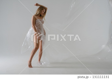 Elegant blonde woman in beauty shoot with plastic draping in studio setting 131111131
